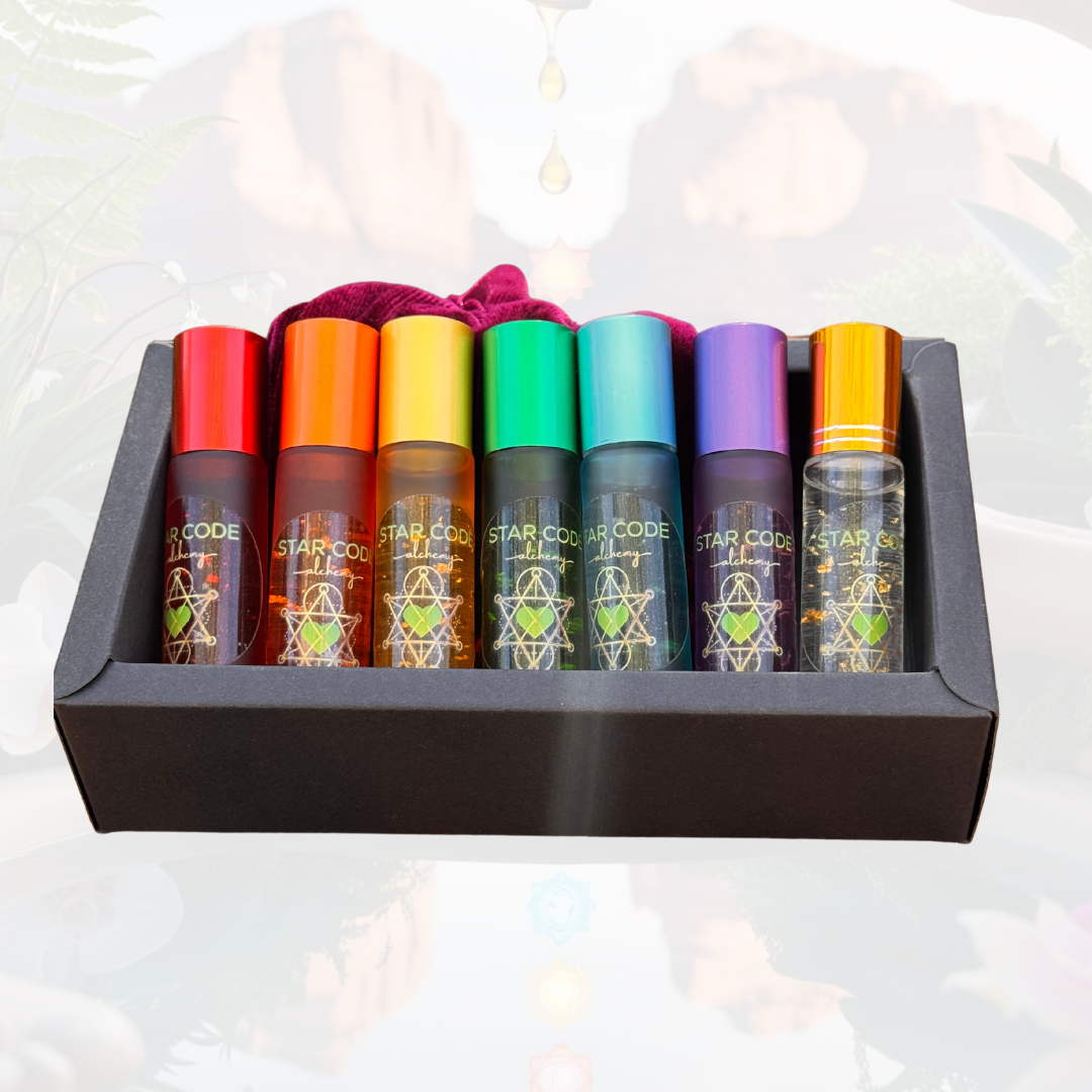 A set of seven colorful roller bottles with essential oils, each labeled with different chakra names and placed in a black box against a backdrop featuring a Sedona landscape. A drop of oil is depicted above the set, suggesting use or evaporation.