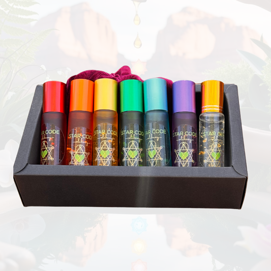 A set of seven colorful roller bottles with essential oils, each labeled with different chakra names and placed in a black box against a backdrop featuring a Sedona landscape. A drop of oil is depicted above the set, suggesting use or evaporation.